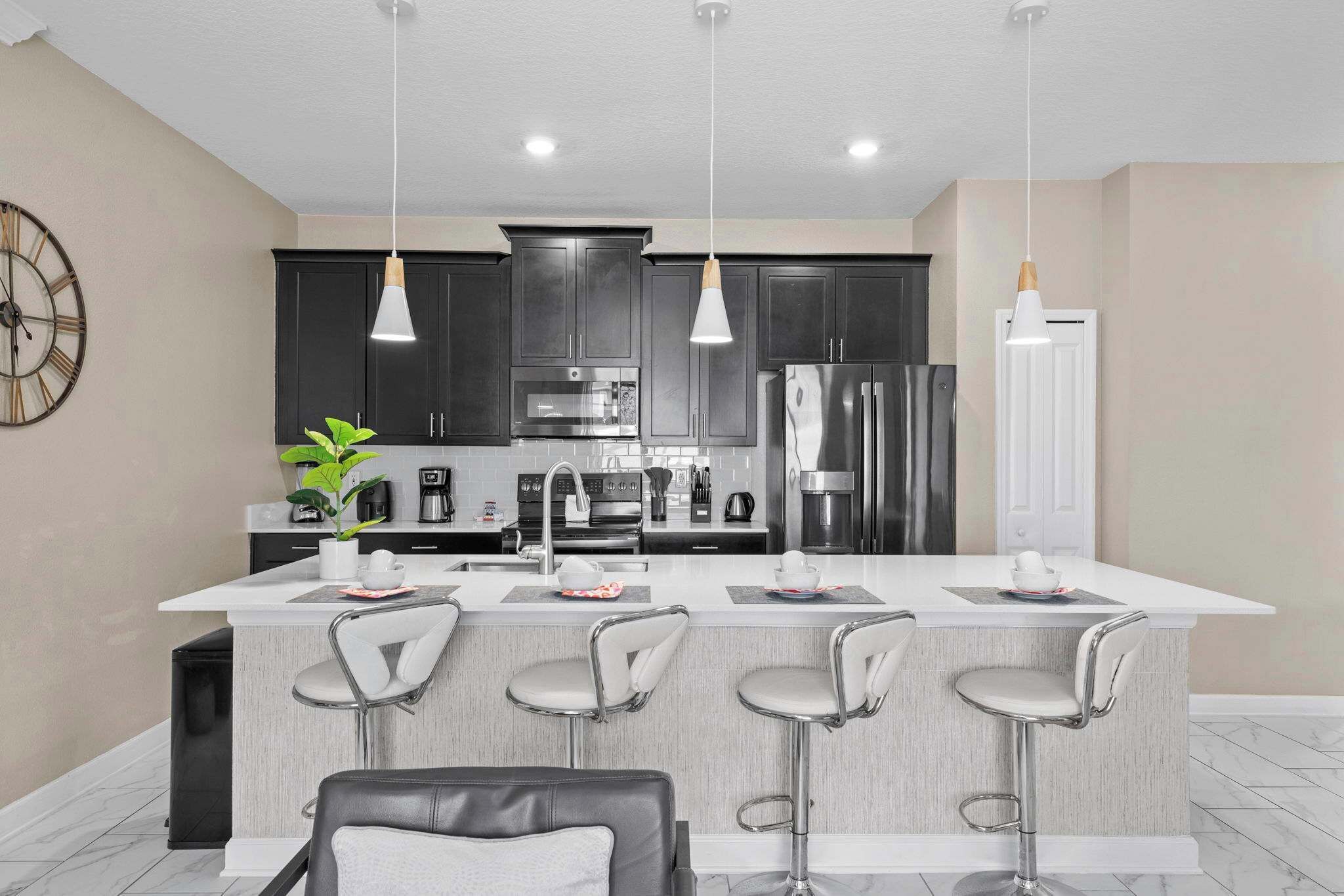 Una cocina moderna con armarios oscuros, una isla central con taburetes de bar e iluminación colgante.
