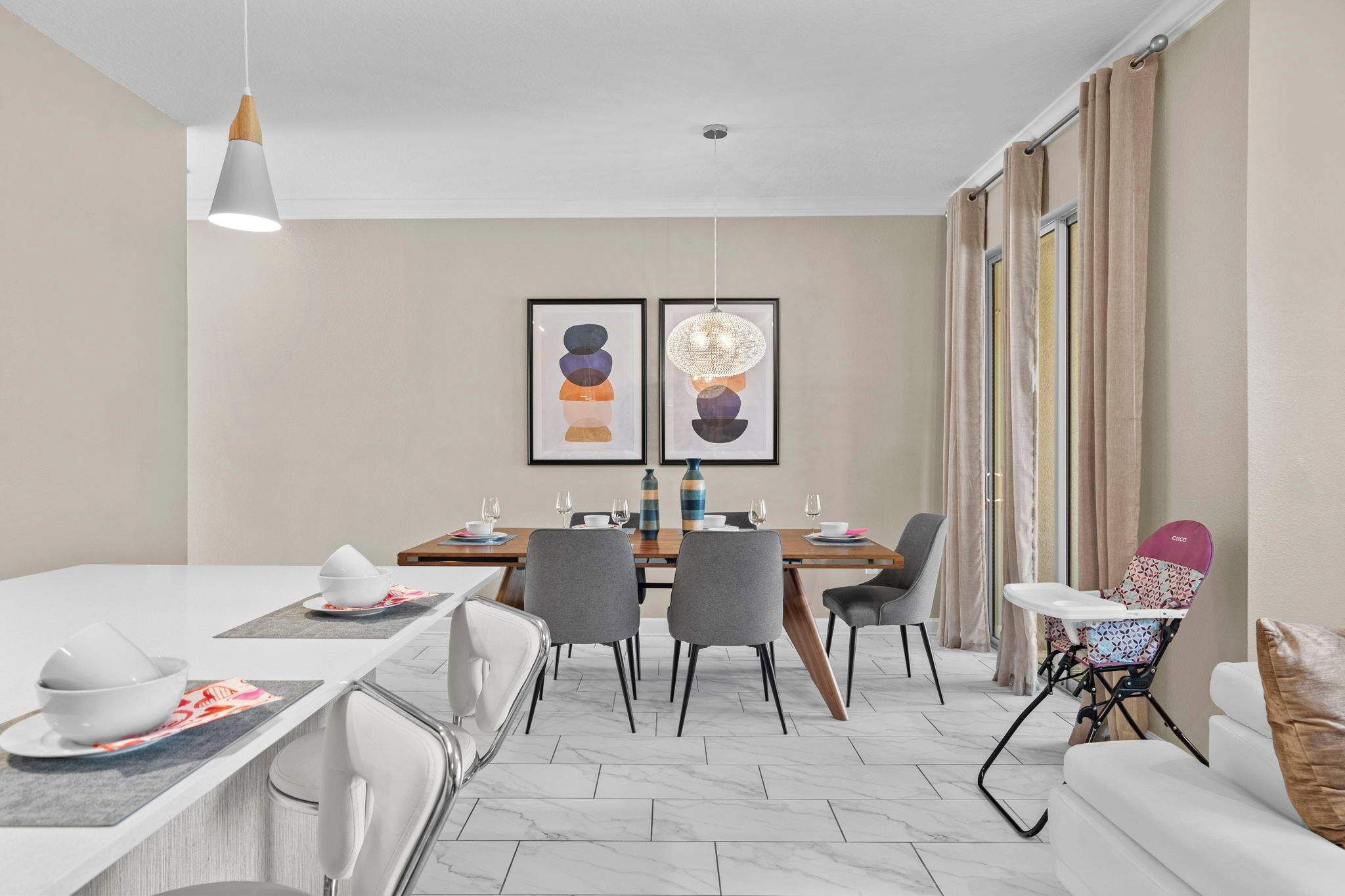 A modern dining area with a table set for four, chairs, a high chair, and a sofa.