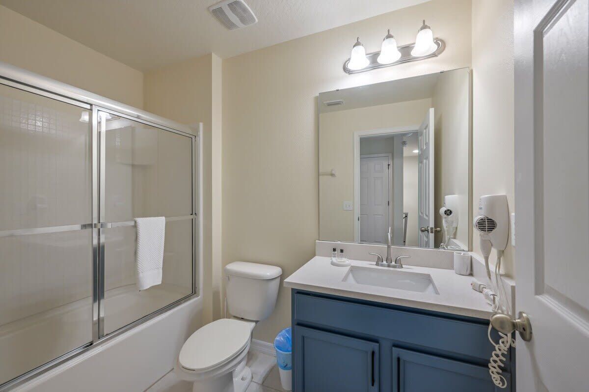 A bathroom with a glass shower enclosure, a white toilet, a sink with a mirror, and a hairdryer on the wall.