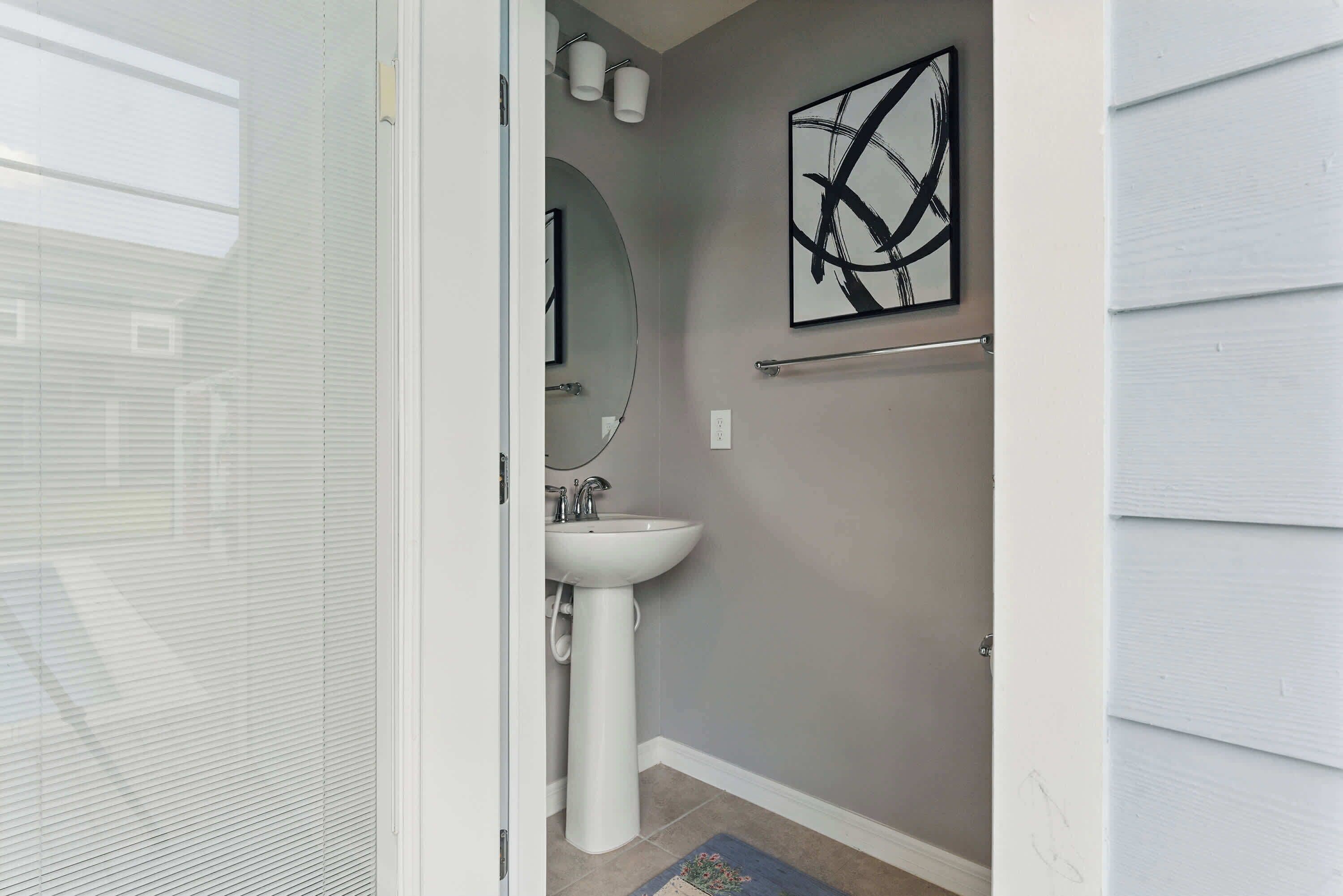 A bathroom with a white sink, a round mirror, and a wall-mounted abstract art piece.