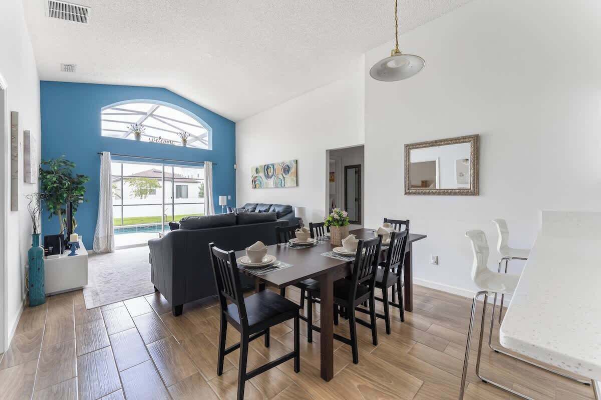 A modern living room with a dining area, featuring a large window, a sofa, and a dining table with chairs.