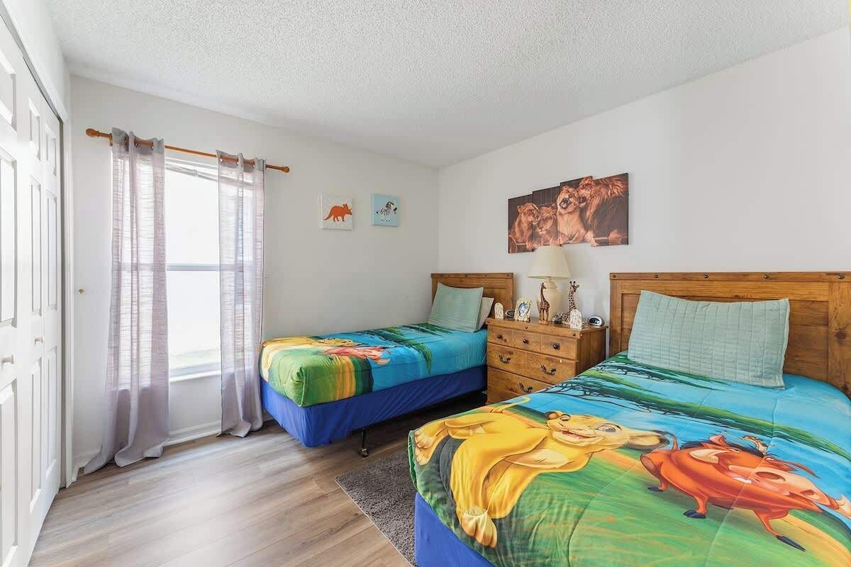 A bedroom with two beds, a wooden headboard, a nightstand, and a window with sheer curtains.
