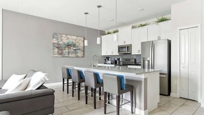 Una cocina moderna con armarios blancos, electrodomésticos de acero inoxidable y un sofá gris con cojines azules.