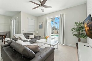 A modern living room with a sofa, coffee table, and a ceiling fan. - Relax Near Disney, 4BR Home With Pool (Kissimmee)