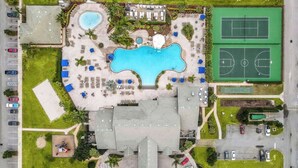 Luchtbeeld van een resort met een zwembad, tennisbanen en een gebouw met een plat dak.