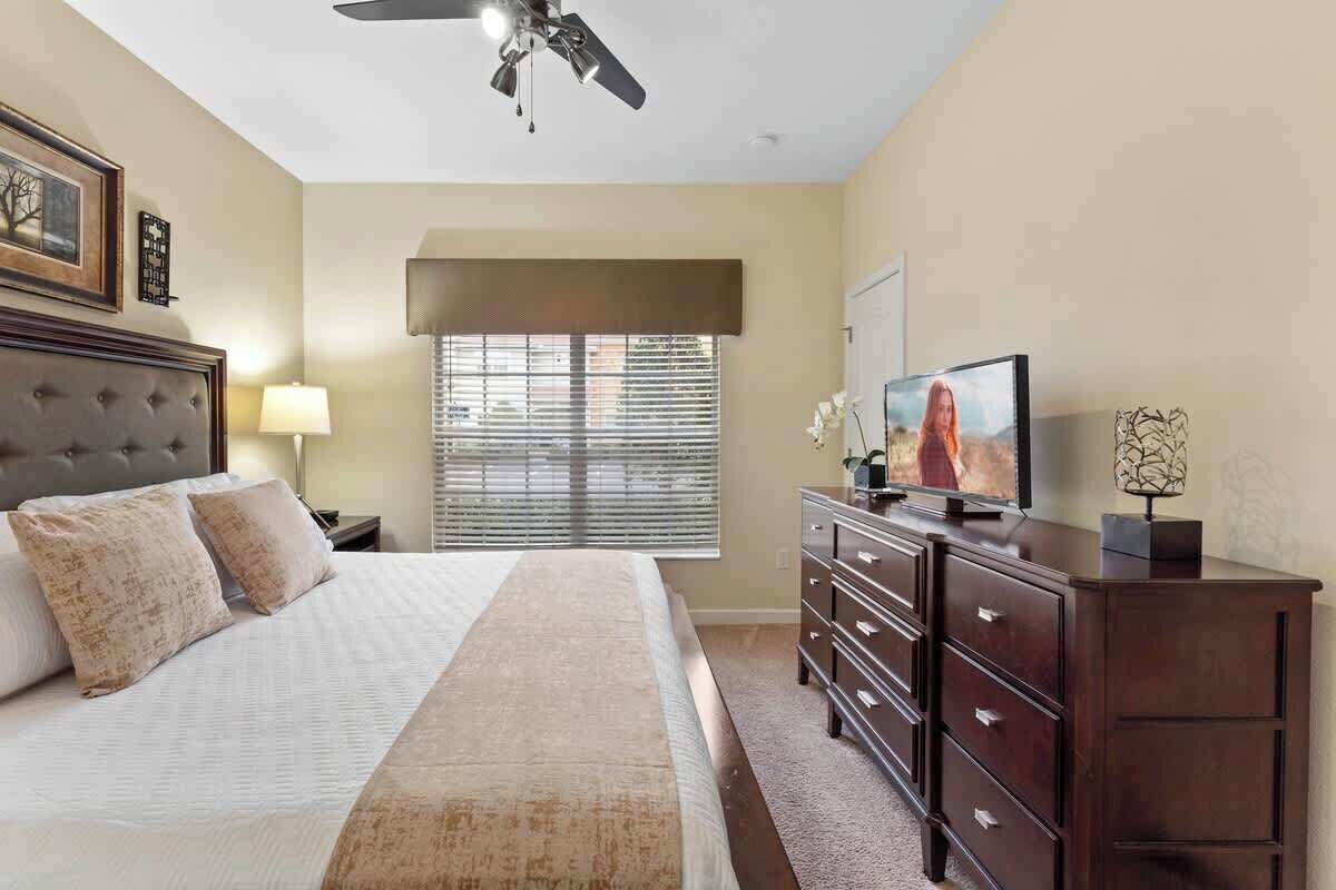 Un dormitorio con cama, cómoda, televisor y ventilador de techo.