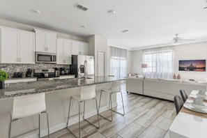 A modern kitchen with white cabinets, a granite countertop, and stainless steel appliances. There is a dining area with a white table and chairs. - Private Pool Plus 5BR Themed Bedrooms (Kissimmee)