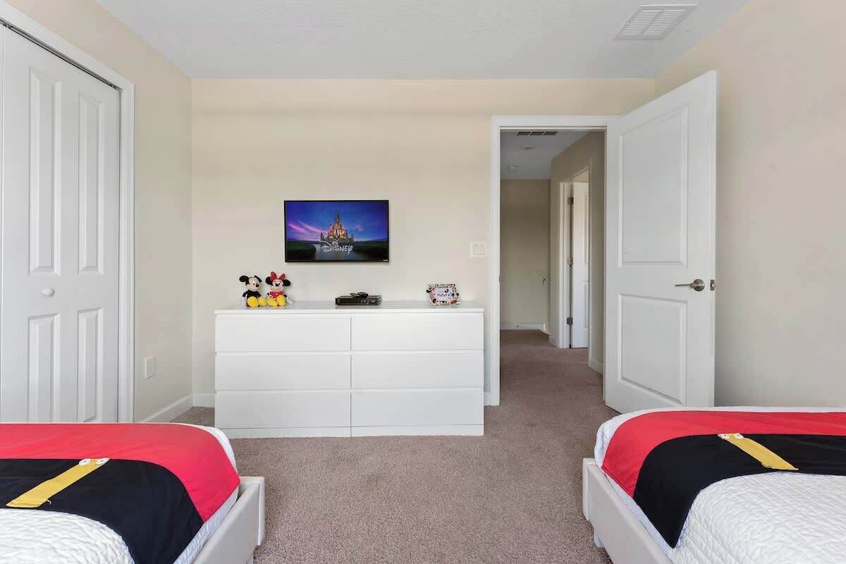 Un dormitorio con dos camas, un aparador blanco y un cuadro con temática de Disney.