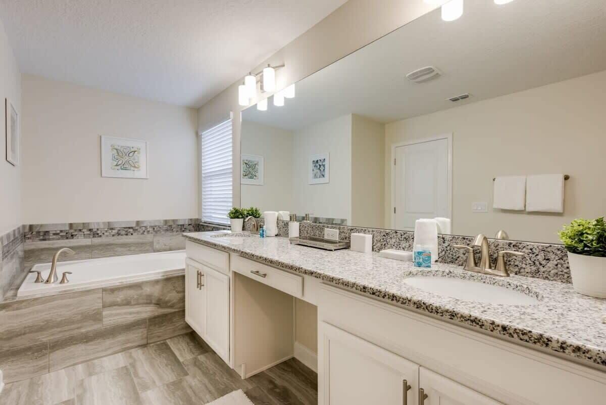 A bathroom with a large mirror, a bathtub, a sink, and a vanity.