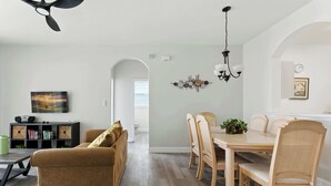 A modern living room with a sofa, dining table, chairs, and a ceiling fan. - Resort Condo 3BR - Pool, Balcony, Near Disney (Kissimmee)