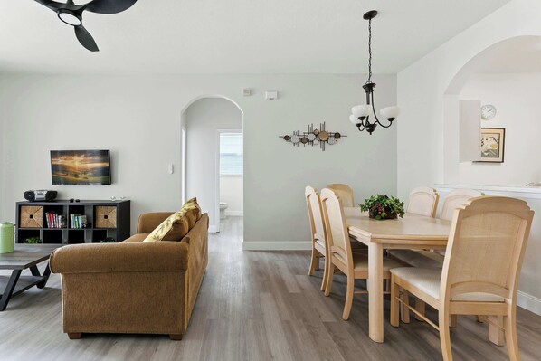 Una sala de estar moderna con sofá, mesa de comedor, sillas y un ventilador de techo.