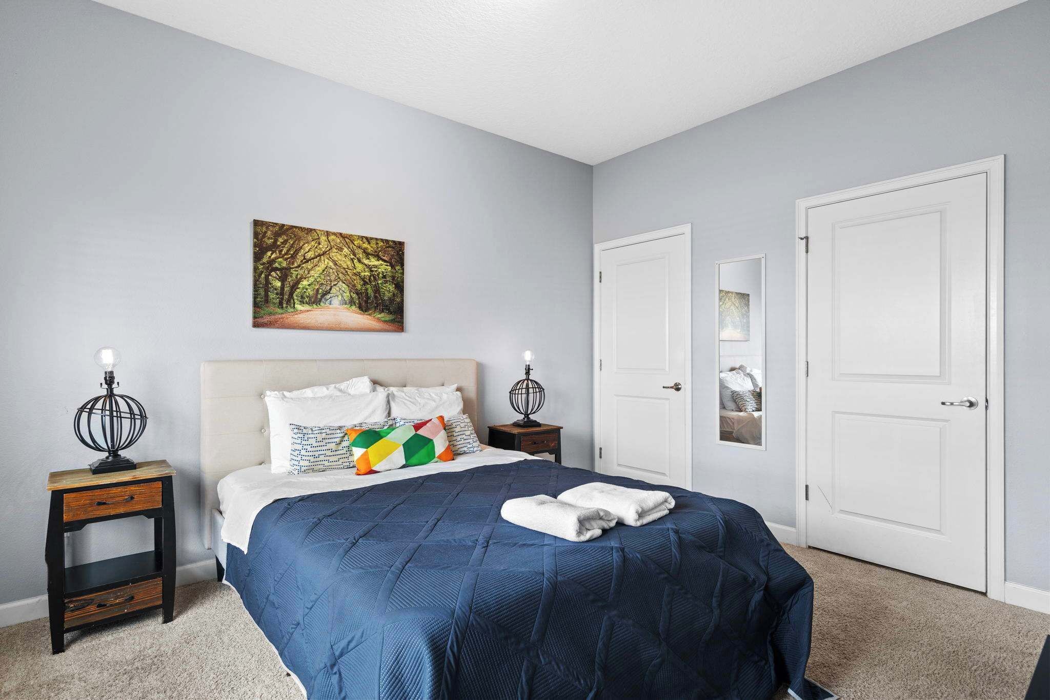 A bedroom with a bed, two nightstands, a painting, and two doors.