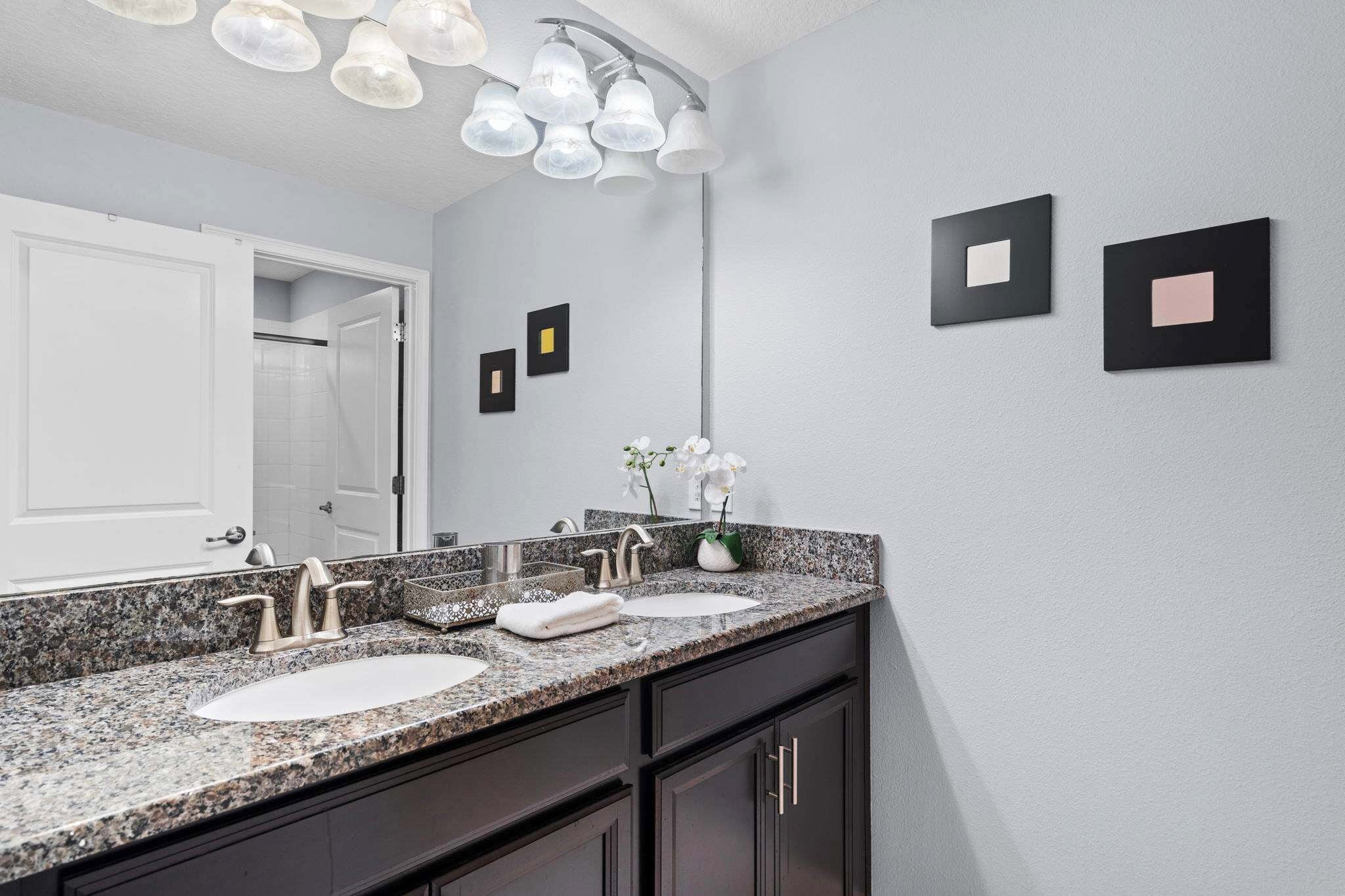 A bathroom with a granite countertop, two sinks, a mirror, and a shower door.