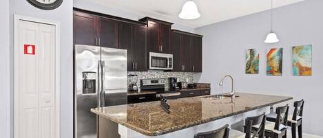 Cocina moderna con alacenas de madera oscura, electrodomésticos de acero inoxidable, encimeras de granito y una isla central con taburetes de bar.