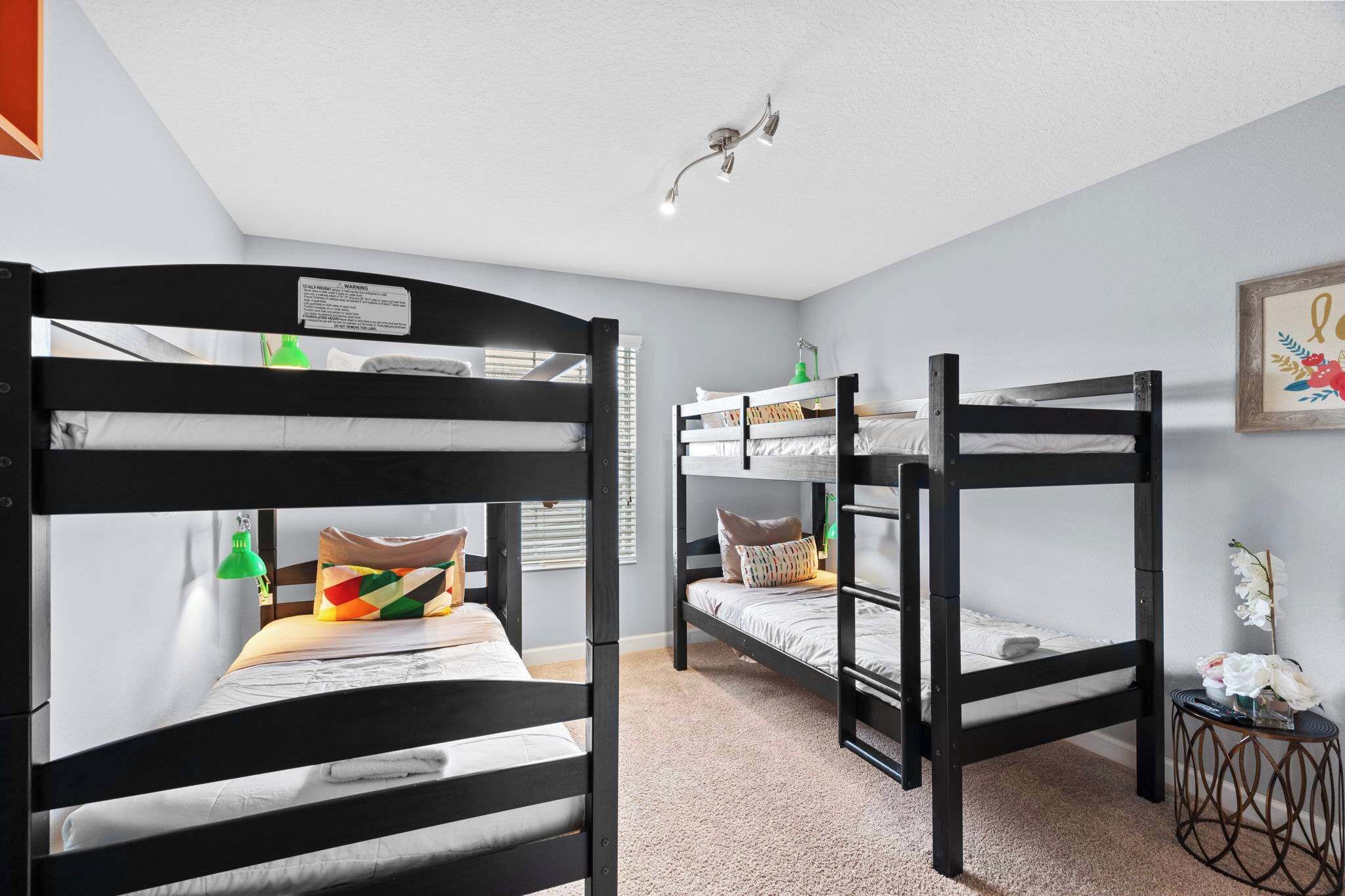 Ein Zimmer mit Etagenbetten, einem kleinen Tisch mit Lampe und einem gerahmten Bild an der Wand.