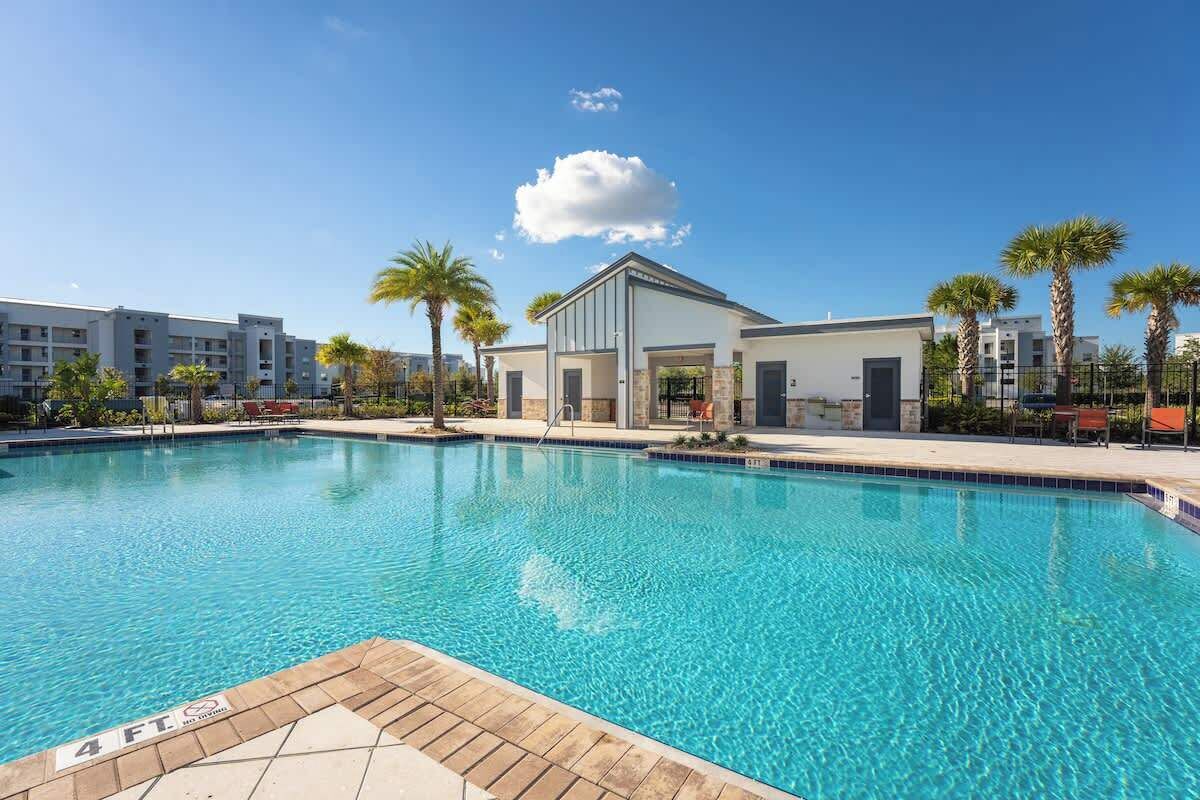 Une piscine à l’eau d’un bleu limpide, entourée de palmiers et bordée d’un bâtiment à toit plat.