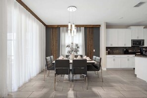A modern dining area with a table set for four, a chandelier, and a view of the kitchen. - Sophisticated 6BR at Storey Lake (Kissimmee)