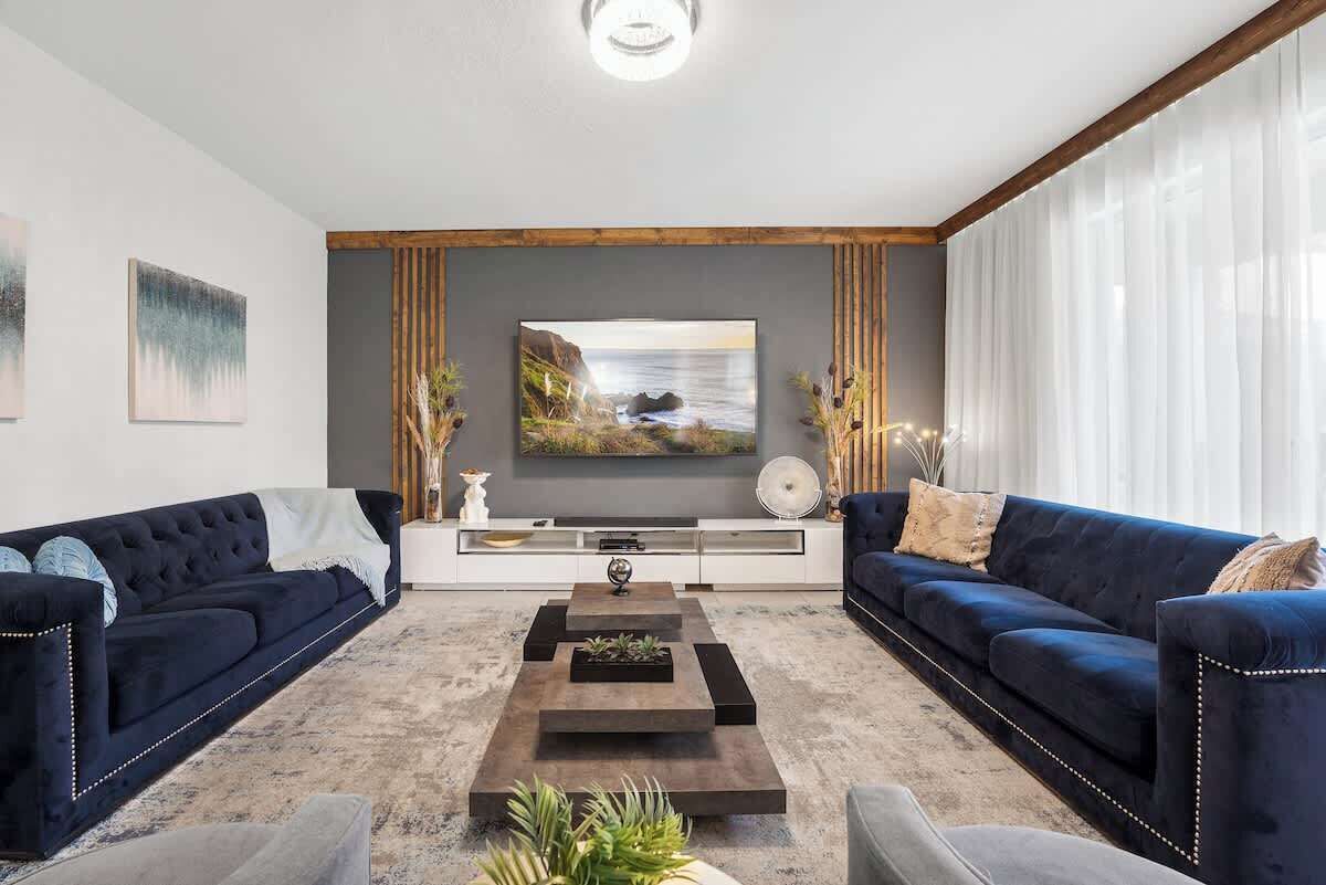 Ein modernes Wohnzimmer mit zwei dunkelblauen Sofas, einem zentralen Couchtisch und einem großen Flachbildfernseher an der Wand.
