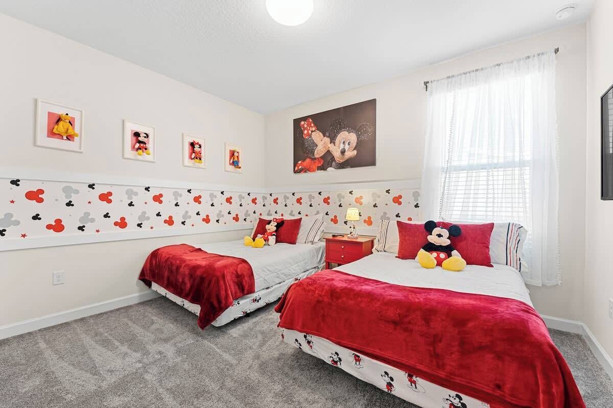 Une chambre avec deux lits, chacun agrémenté de linge de lit aux motifs de Mickey Mouse, un doudou à l’effigie de Mickey Mouse sur le plus grand lit, et des décorations murales représentant Mickey Mouse.