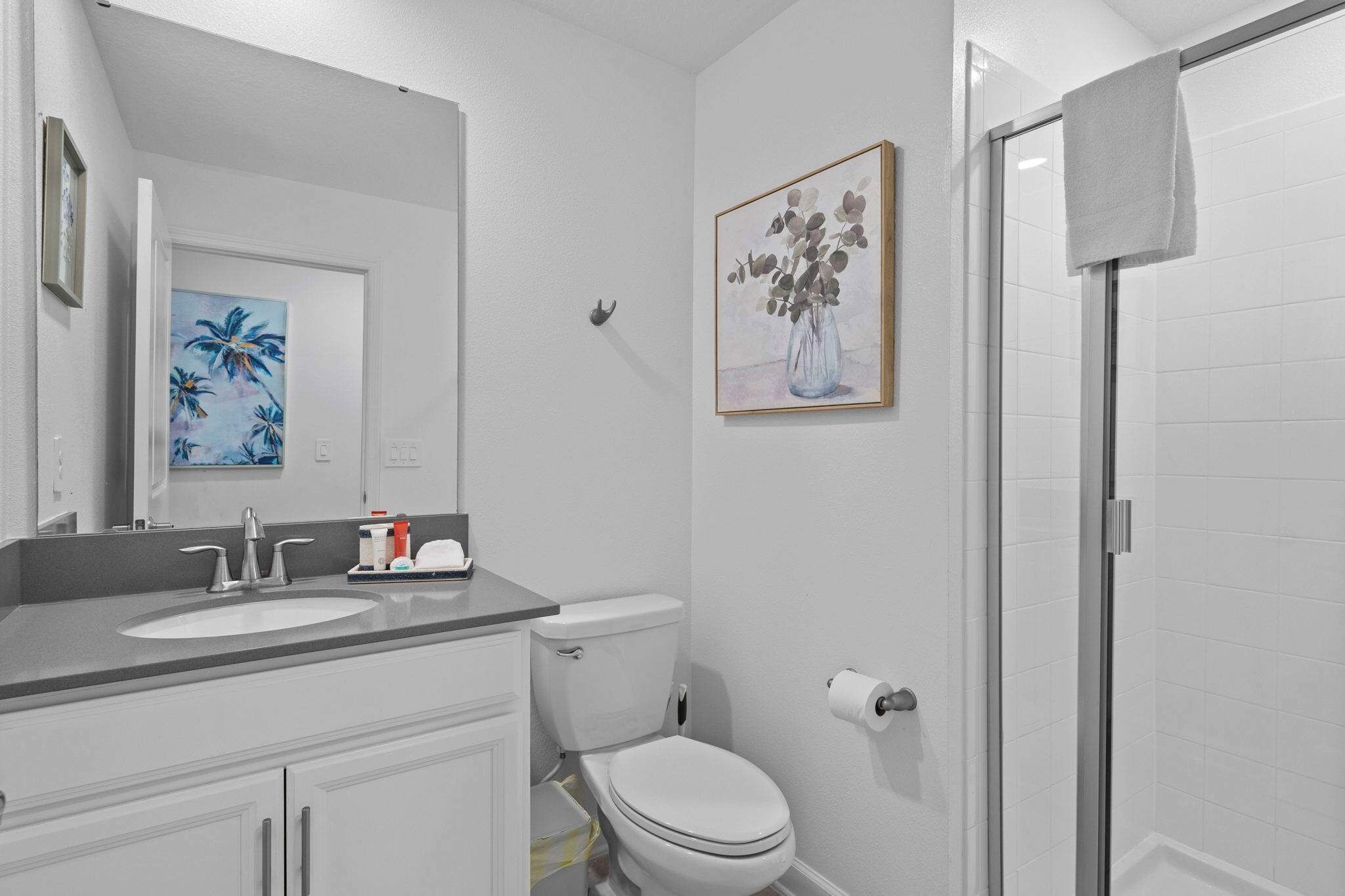 Un baño con lavamanos, inodoro y ducha blancos. Hay dos cuadros en la pared.