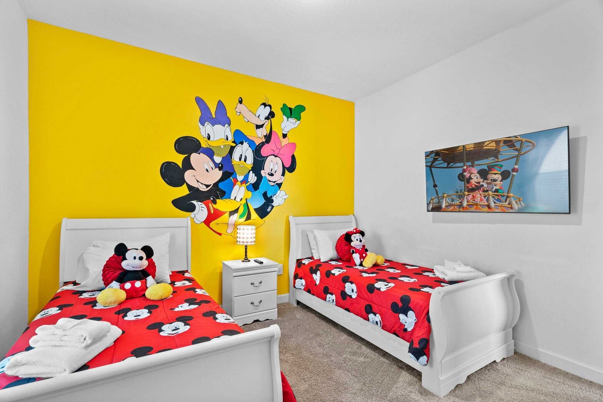 Quarto com duas camas, cada uma com colcha temática do Mickey Mouse, um mural grande do Mickey Mouse na parede e uma foto emoldurada de Mickey e Minnie na parede oposta.