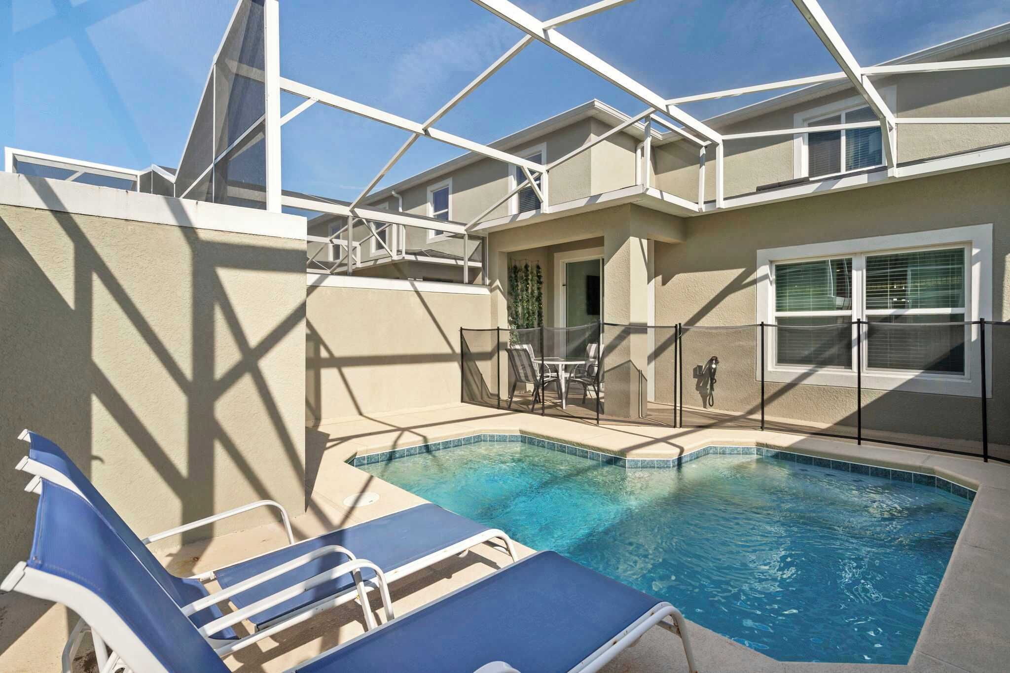 A swimming pool with lounge chairs, a covered patio, and a building with a balcony.