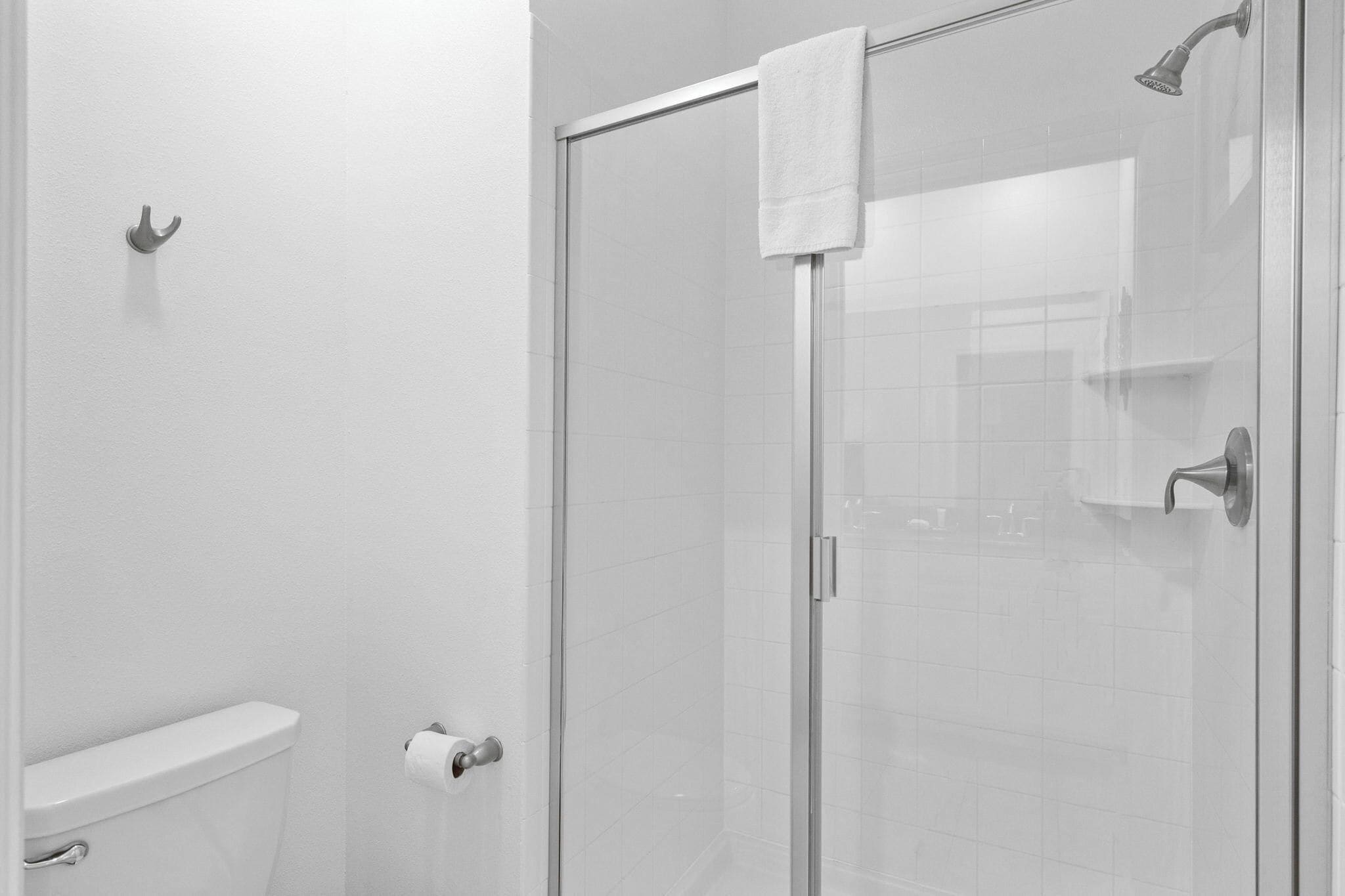 A bathroom with a toilet, a shower with a glass door, and a towel hanging on the shower door.