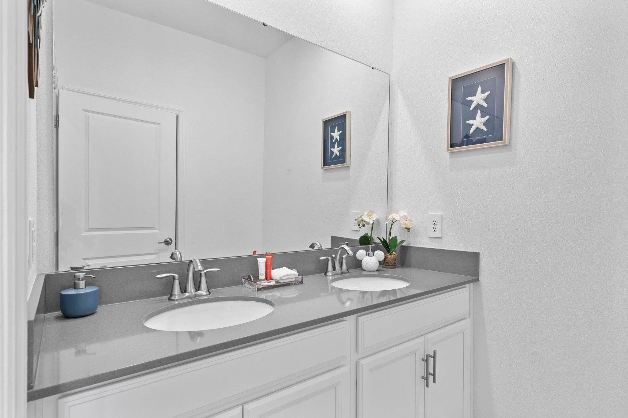 A bathroom with two sinks, a large mirror, and framed artwork on the wall.