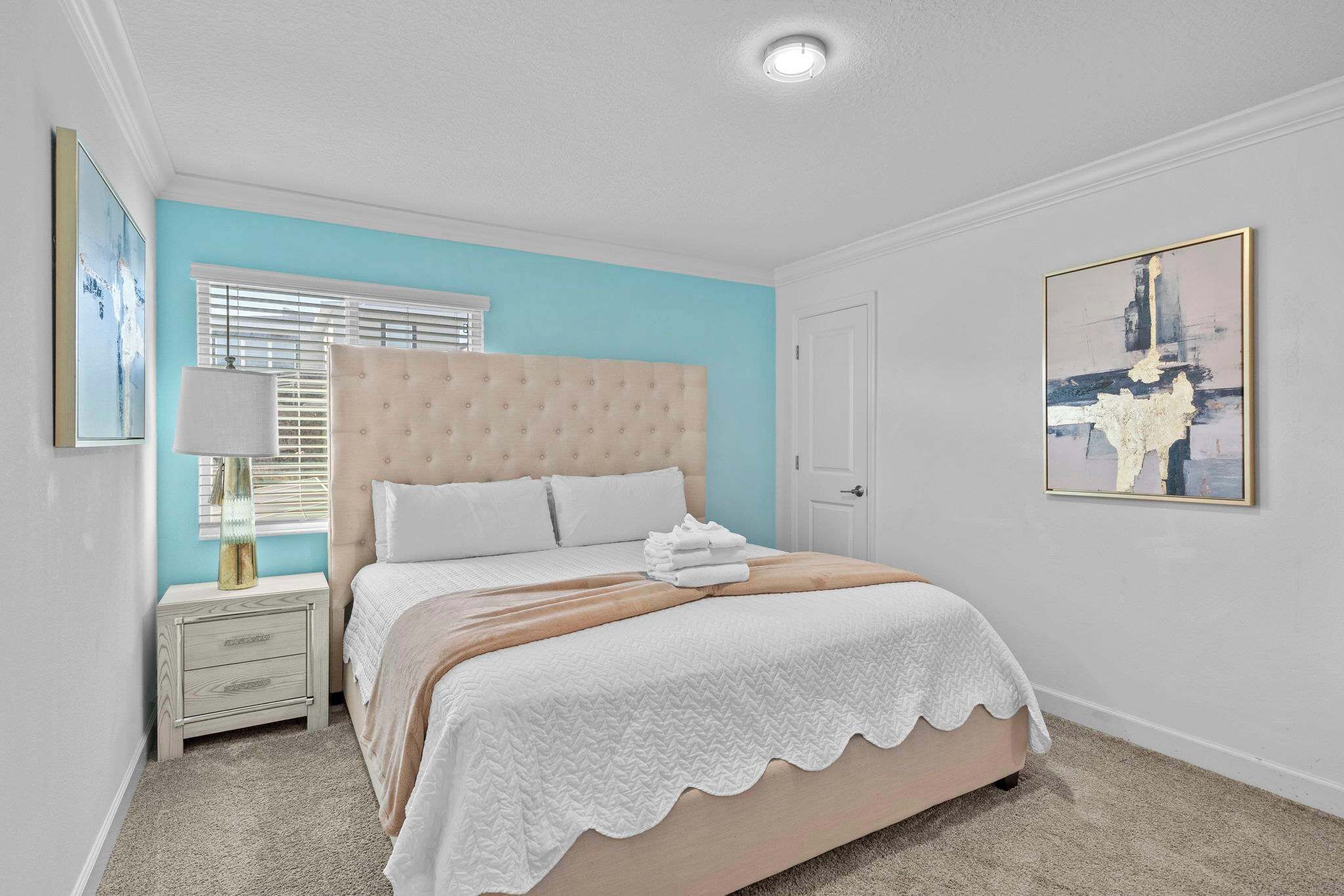 A bedroom with a bed, a nightstand, a lamp, and a painting on the wall.