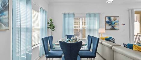 Un comedor con una mesa de vidrio, sillas azules y un sofá con cojines.