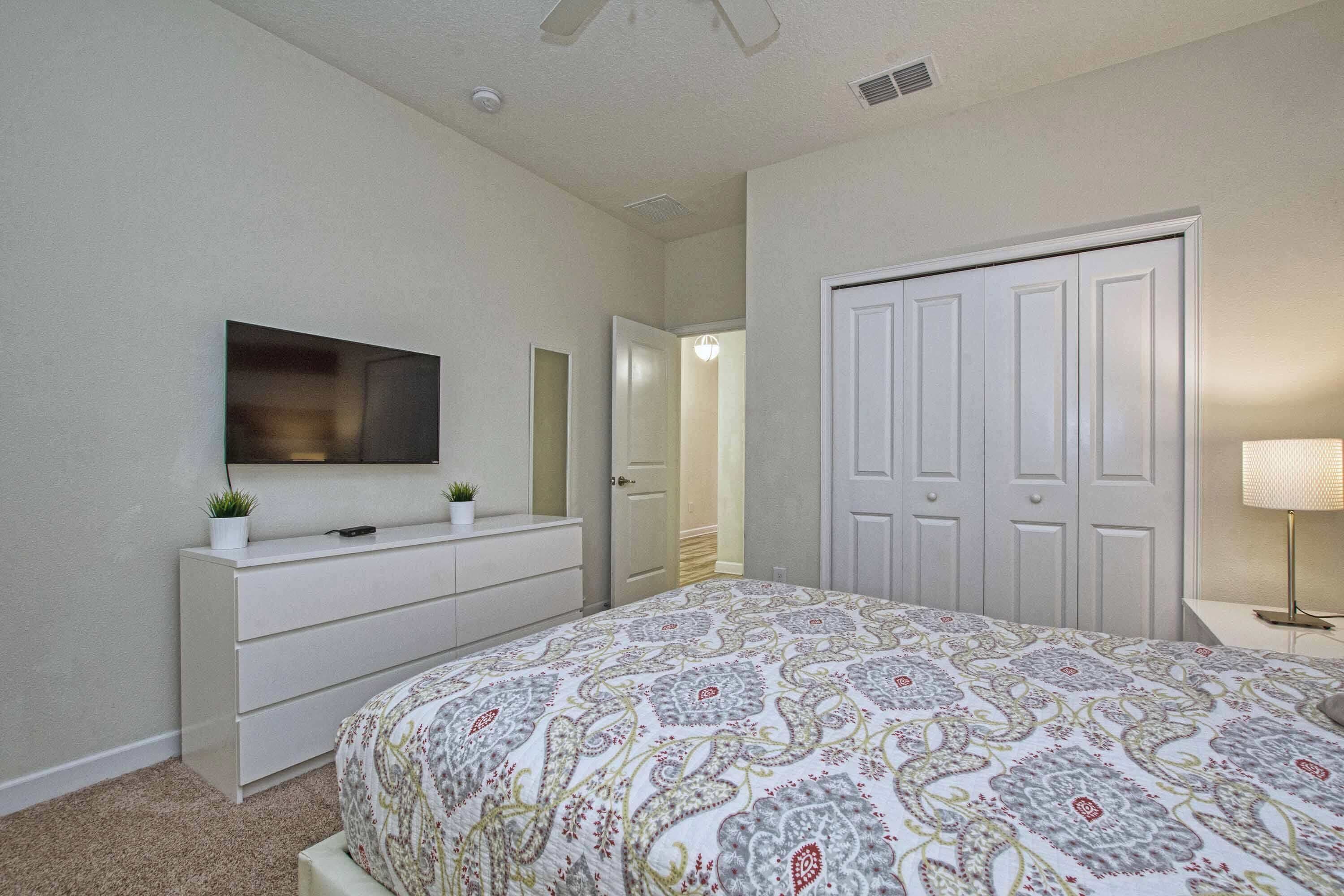 A bedroom with a bed, a dresser, a TV, a closet, and a lamp.