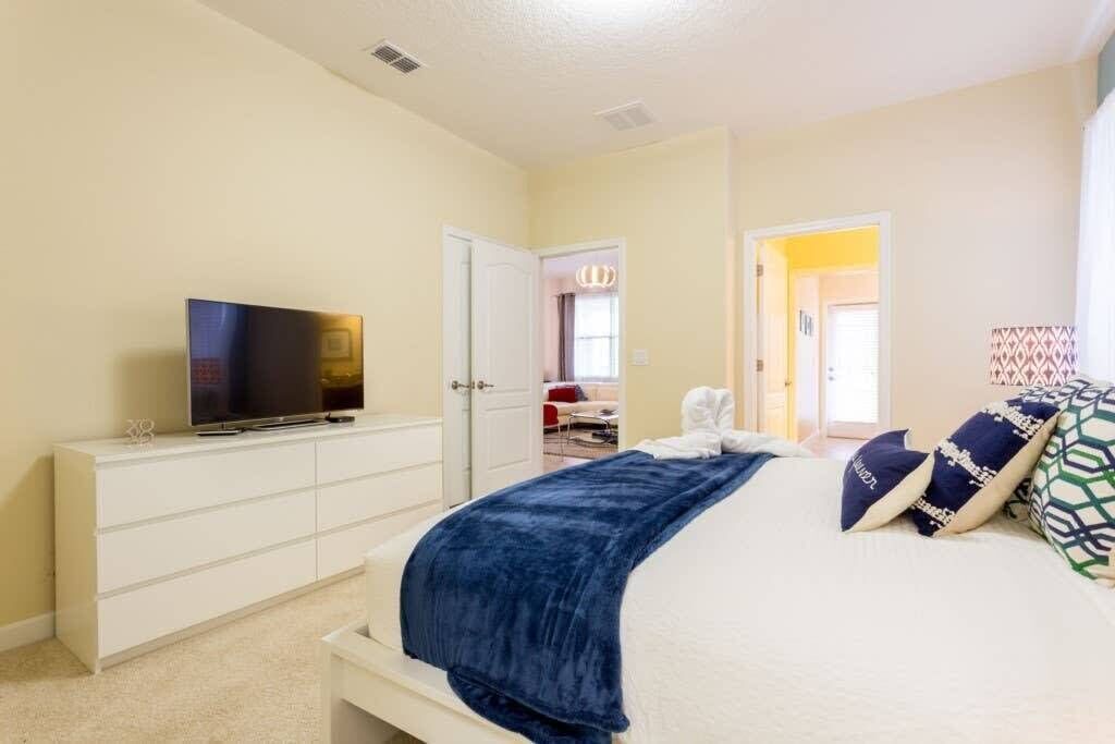 Ein Schlafzimmer mit einem Bett, einem Fernseher auf einer Kommode und einer Tür zu einem anderen Raum.