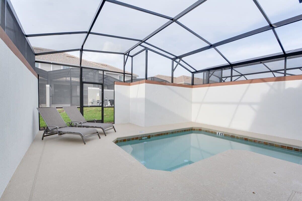 Une piscine entourée de parois en verre, deux chaises longues et, au loin, une maison qui se profile à l’horizon.