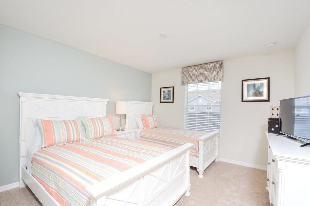 A bedroom with a bed, bedside tables, a dresser, a television, and a window with blinds.