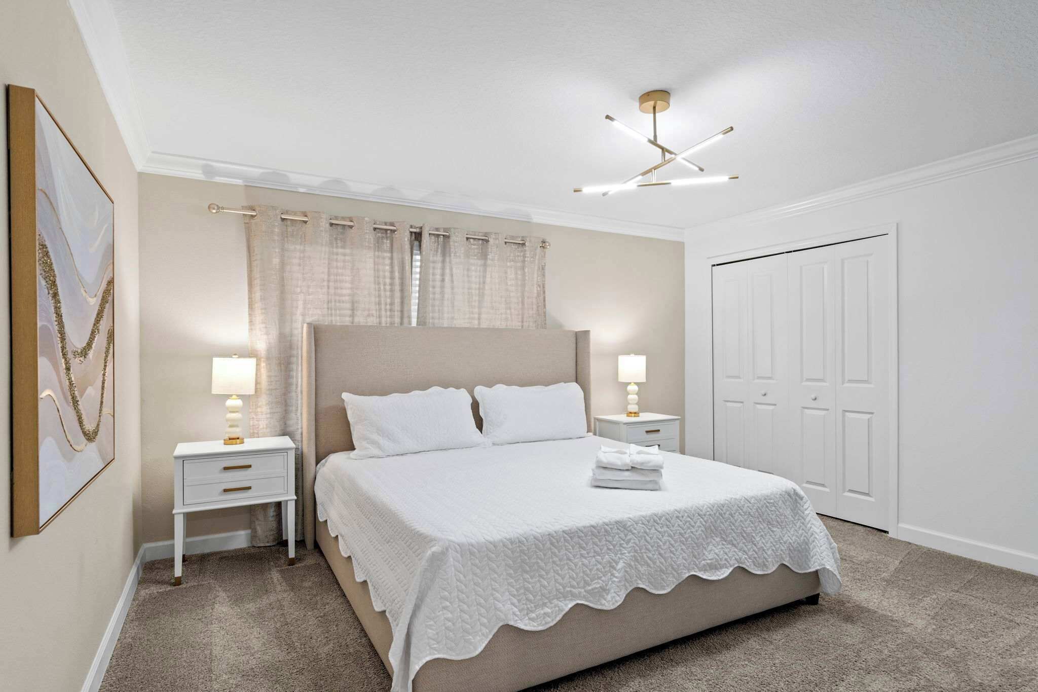 A bedroom with a bed, nightstands, a ceiling light fixture, a door, and a framed picture on the wall.