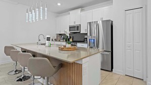 Une cuisine moderne avec des meubles blancs, un réfrigérateur en acier inoxydable, un four à micro-ondes et un îlot central intégré avec des tabourets de bar.