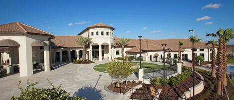 A spacious courtyard with a central fountain, surrounded by palm trees and a white building with arched walkways.