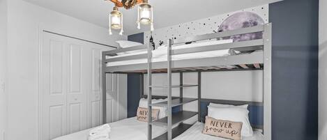 Une chambre avec un lit superposé, du linge de lit blanc, un luminaire en bois au plafond et un autocollant représentant la lune sur le mur.