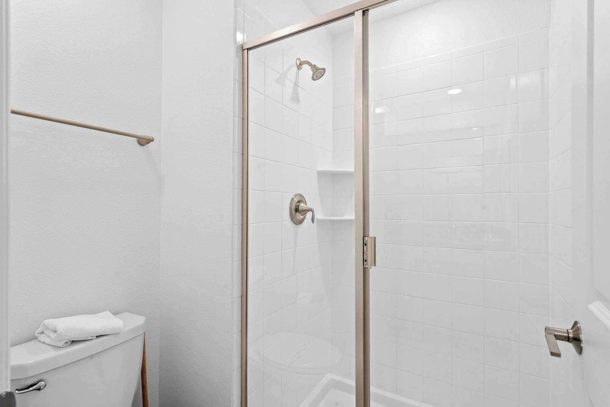 A bathroom with a toilet, a towel rack, a shower with a glass door, and white tiled walls.