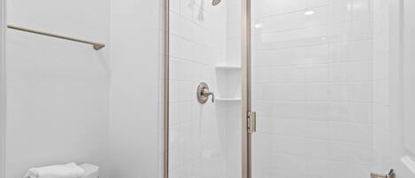 A bathroom with a toilet, a towel rack, a shower with a glass door, and white tiled walls.