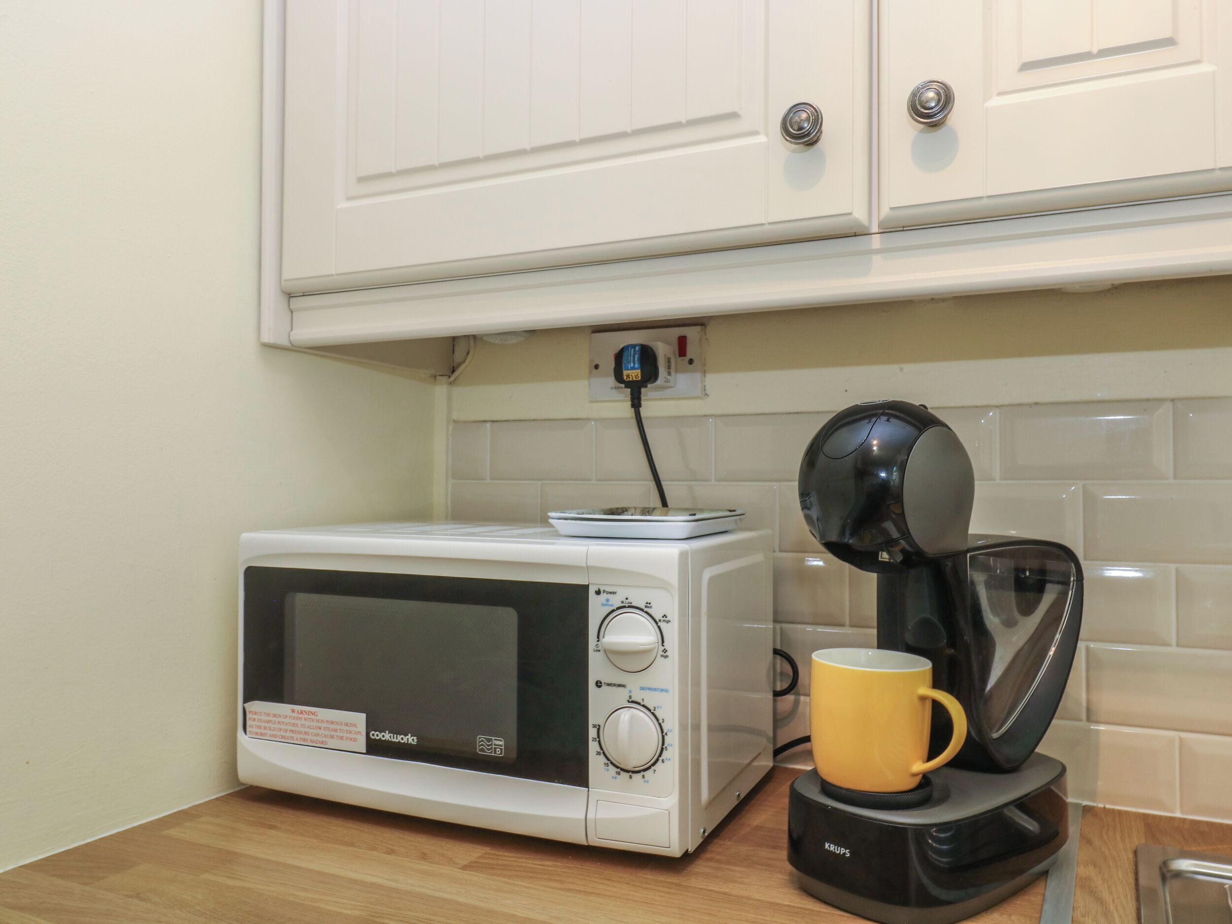 Une cuisine équipée d’un four à micro-ondes, d’une machine à café et d’une tasse jaune posée sur le comptoir.