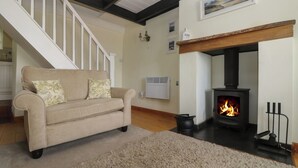 Una sala de estar con un sofá color crema, una chimenea, una escalera y una pared blanca con un cuadro.