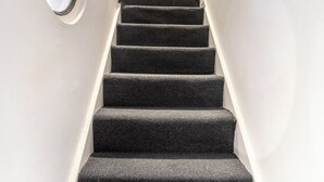Un escalier dont les marches sont recouvertes de moquette et un grand miroir rond fixé au mur.