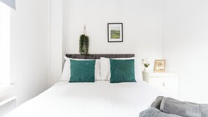 Une chambre à coucher avec un lit, des murs blancs, un tableau accroché au mur et une plante.