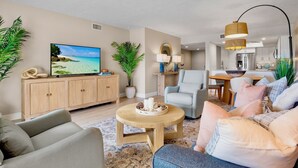 A modern living room with a flat-screen TV, a wooden coffee table, a grey sofa, and a light blue armchair. - Midnight Cove II – Unit 133 (Siesta Key)