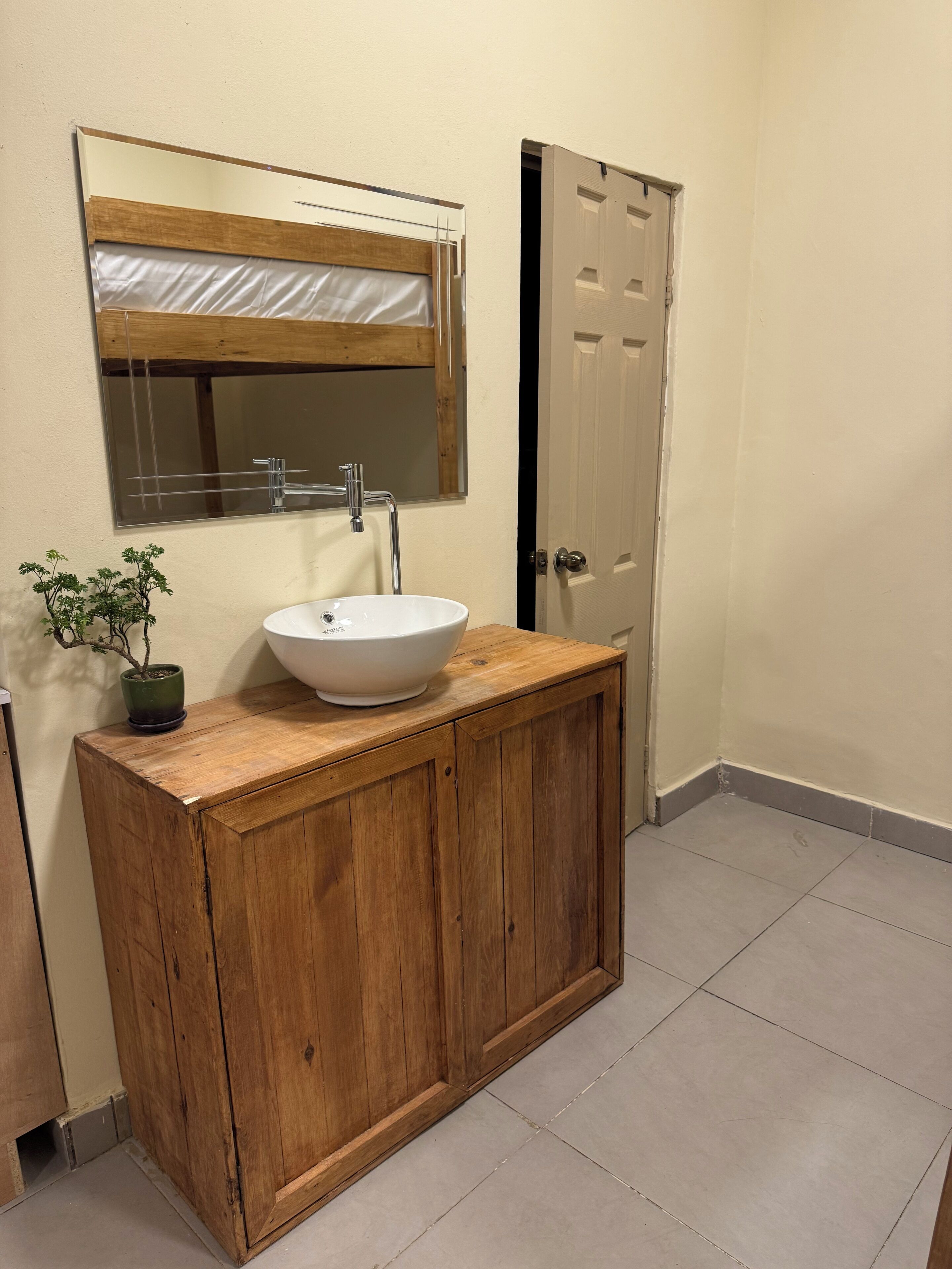 A bathroom with a wooden vanity, a white sink, a mirror, and a potted plant.