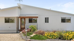 A modern single-story house with a white exterior, a front porch, and a small garden with yellow flowers. - Scarp n Sea – Sauna, Views & Serene Coastal Escape (Falcon)