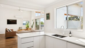 Eine moderne Küche mit weißen Schränken, einem großen Fenster und einem Essbereich mit einer braunen Ledersofa.