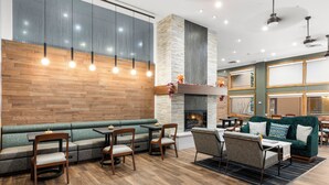 Ein moderner Lounge-Bereich mit Kamin aus Naturstein, Holzboden und verschiedenen Sitzgelegenheiten, darunter eine Couch, Sessel und ein Tisch.