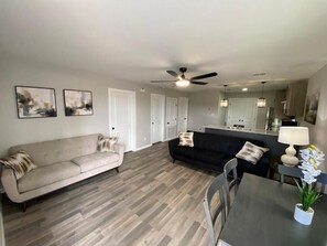 A living room with a beige sofa, a black sofa, and a dining table with chairs. There is a ceiling fan, a lamp, and a small plant on the table. - Executive Suite (Weslaco)